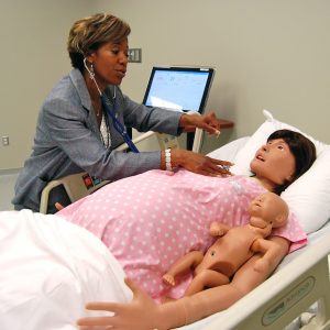 Dr. Rhonda Edison, a board member of the Arkansas Colleges of Health Education and physician in Pea Ridge, Ark., demonstrates how students will work with “Lucy,” a pregnancy simulator.